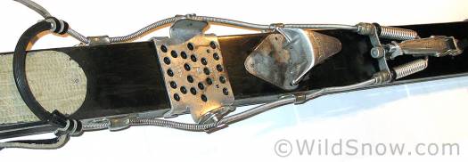 This is an unusual binding setup. It's a cable binding circa 1950 with a releasable toe, only in this photo it is configured with a touring adapter "toe iron" that hooked on to the ski behind the release toe. As shown, the adapter is farther back than its intended location, but you get the idea. At first I thought the adapter was a home made job, but it appears to be something that was manufactured. Click here to enlarge image. This is an unusual binding setup. It's a cable binding circa 1950 with a releasable toe, only in this photo it is configured with a touring adapter "toe iron" that hooked on to the ski behind the release toe. As shown, the adapter is farther back than its intended location, but you get the idea. At first I thought the adapter was a home made job, but it appears to be something that was manufactured. Click here to enlarge image.