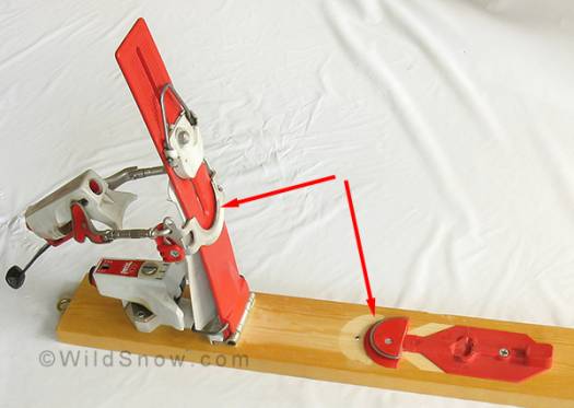 Binding plate raised on touring pivot, showing underside. Arrows indicate half-moon shaped mechanism that engaged to lock the plate down for alpine (latched heel) mode. Conversion between modes requires exiting the binding. V shaped wire near top is the climbing lifter, engaged by flipping down. Binding plate raised on touring pivot, showing underside. Arrows indicate half-moon shaped mechanism that engaged to lock the plate down for alpine (latched heel) mode. Conversion between modes requires exiting the binding. V shaped wire near top is the climbing lifter, engaged by flipping down.