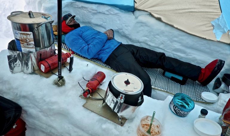 Cal resting in the cook tent while the stoves roar on melting snow for water.