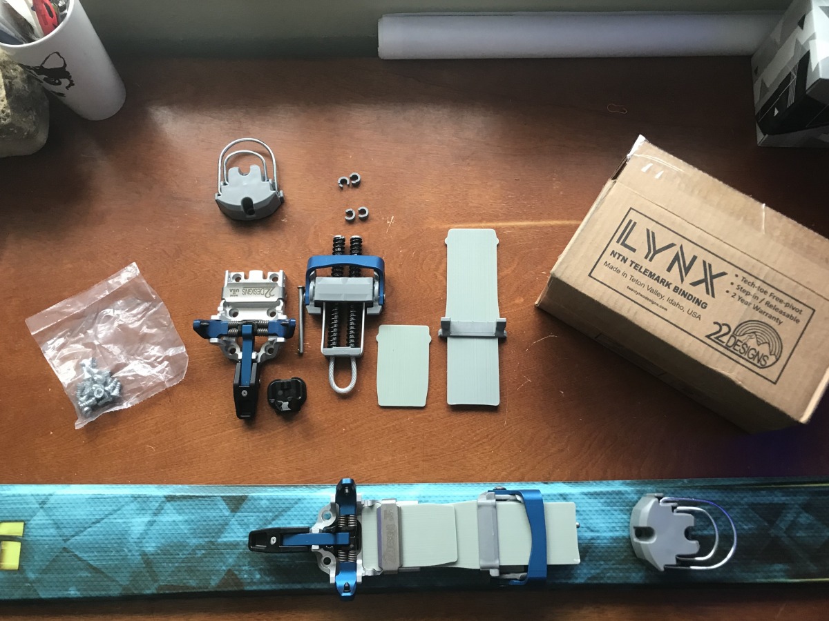 The 22 Designs Lynx in its component pieces, and dry assembled on the ski. The tech toe design, and climbing heel bails are a familiar riff; the innovation in the Lynx is in the combination of composite leaf spring plates, and coil springs. The plates provide the primary resistance, while the main function of the coil springs is to lock in the claw at the 2nd heel. Spacers for the coil springs allow for adjustment of claw tension.