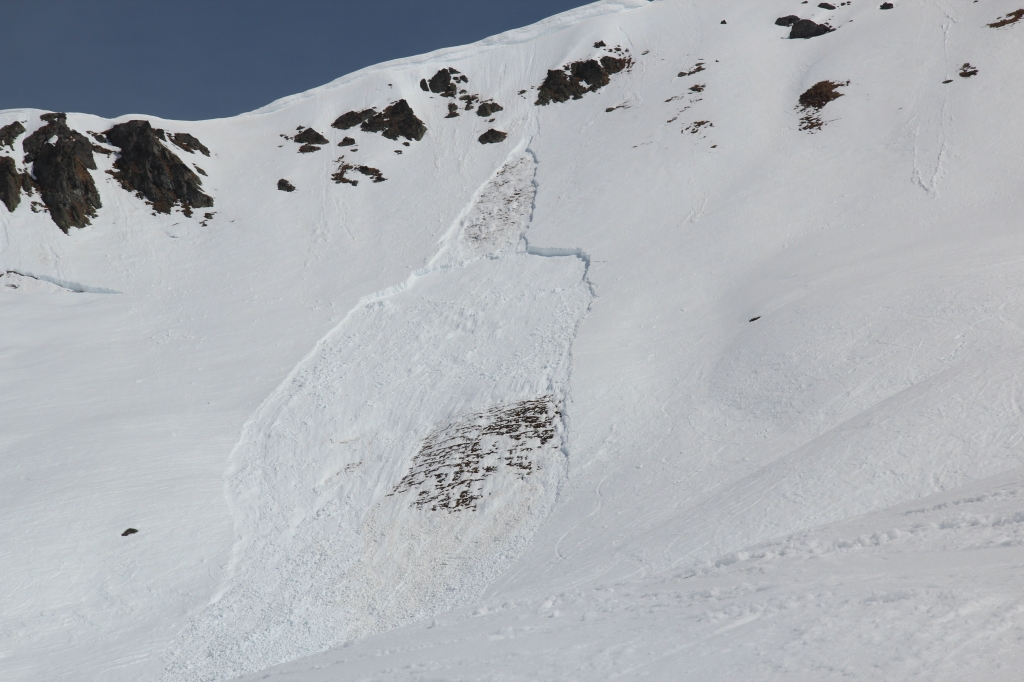 Notice how a loose-wet or point-release avalanche starts off the rocks, then triggers a slab below. Dark-colored rocks absorb sunlight, warming the snow around them. Bonds loosen within the snow, creating a small, loose-wet avalanche. The dense debris rolls downhill and then triggers a slab avalanche on steep, rocky, shallow terrain.