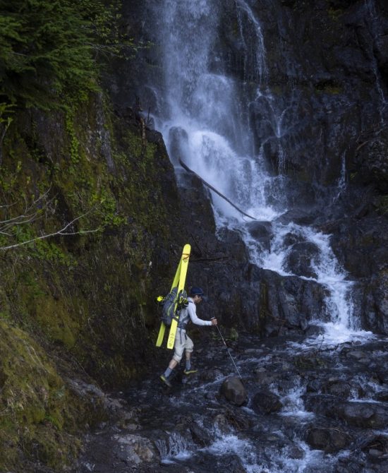 Trevor Kostanich crosses below a cascading waterfall on the Heliotrope Ridge trail during the exit from Mount Baker. Each peak required significant mileage of trail walking before skis could be employed on the glaciers and seasonal snow fields.