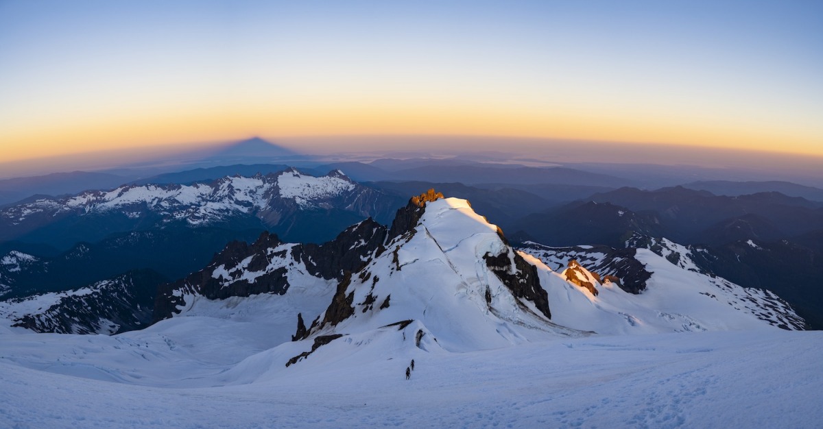 Climbing parties ascending the Roman Wall, the final steep face en route to the summit of Mount Baker, while sunrise lights Colfax Peak below and casts the shadow of Mt. Baker across the San Juan Islands and Puget Sound.